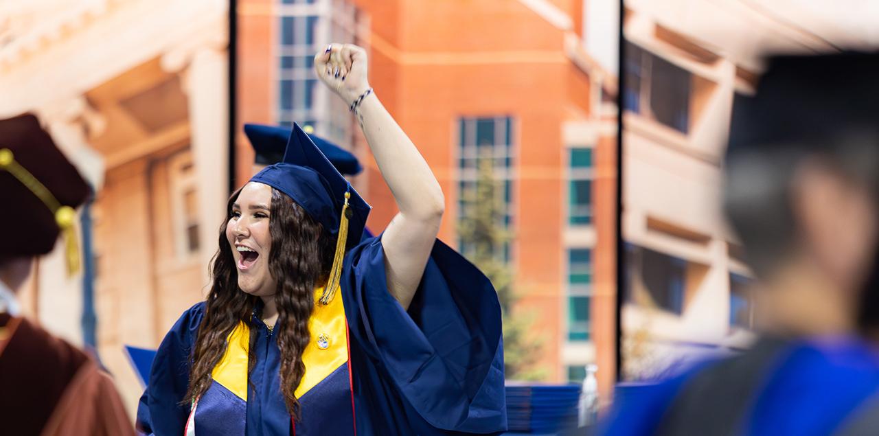 UNC graduate raising their arm 和 smiling during a graduation ceremony.