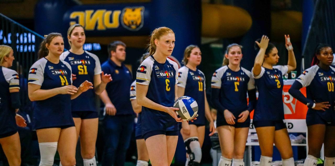 Syd Cole stands with a volleyball in her hands while a row of her teammates stand behind her.